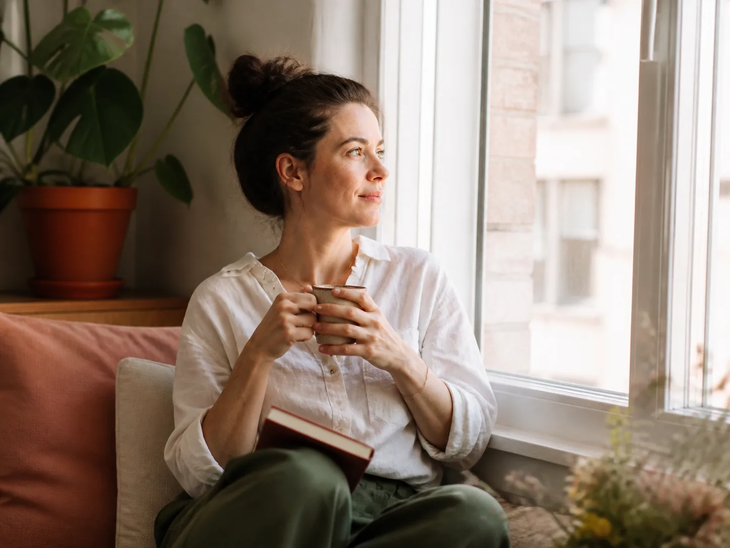 A woman reflecting calmly with a journal by a bright window